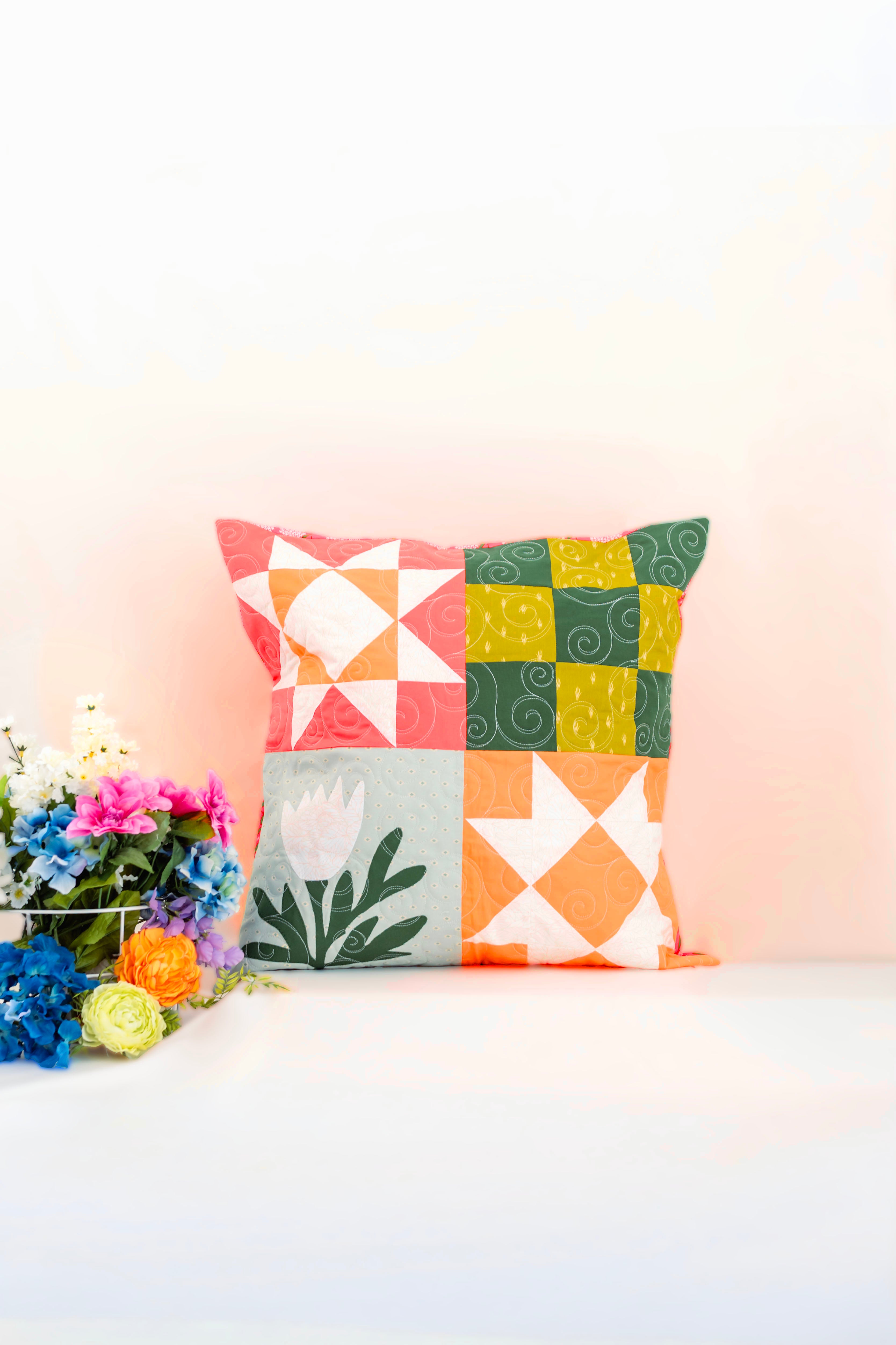 Colorful geometric-patterned pillow on a white surface with flowers in the background