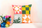 Colorful patchwork pillow on a white surface with flowers in the background