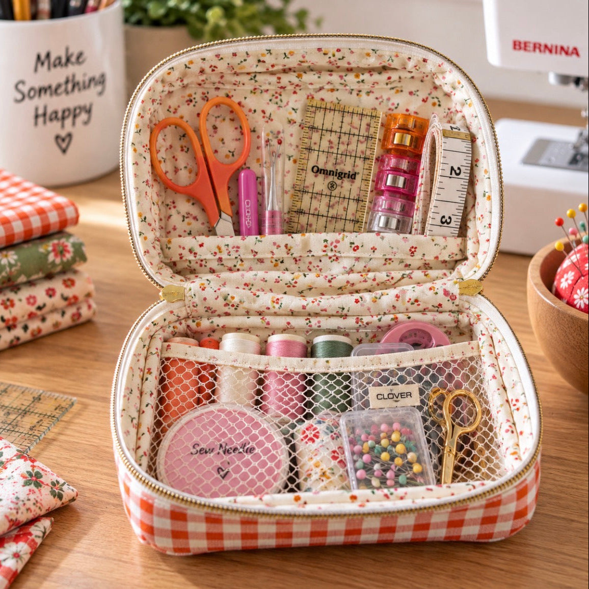 An open floral and gingham storage organizer bag filled with sewing supplies, including scissors, thread, pins, and measuring tools, set on a wooden table with sewing-themed props around it.