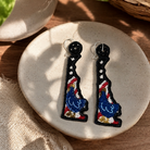 Pair of decorative earrings on a round stone surface with a plant in the background