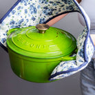 Green Enamelled Cast Iron Casserole Dish held by a person wearing a floral apron.