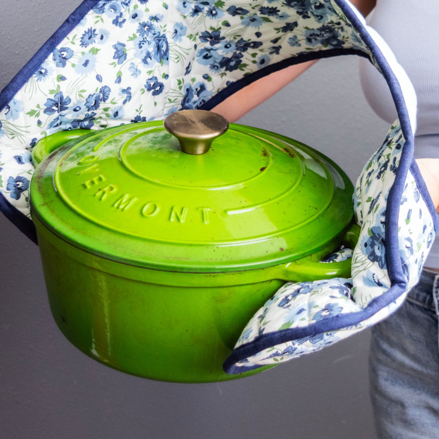 Green Enamelled Cast Iron Casserole Dish held by a person wearing a floral apron.