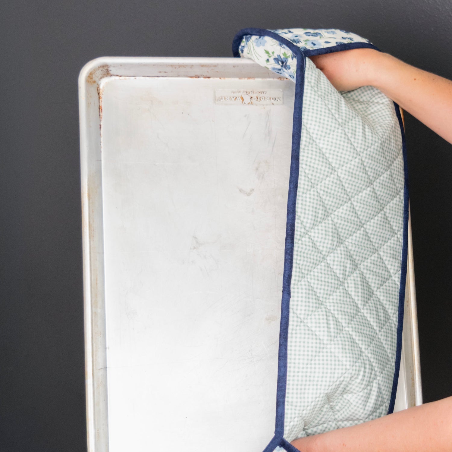 Person holding a baking tray with a quilted cloth on a dark background