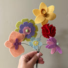 Hand holding a colorful arrangement of felt flowers against a neutral background