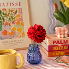 Colorful still life with a mug, flowers, books, and a painting of Matisse.