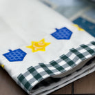 Folded fabric with blue and yellow embroidered designs on a checkered border.