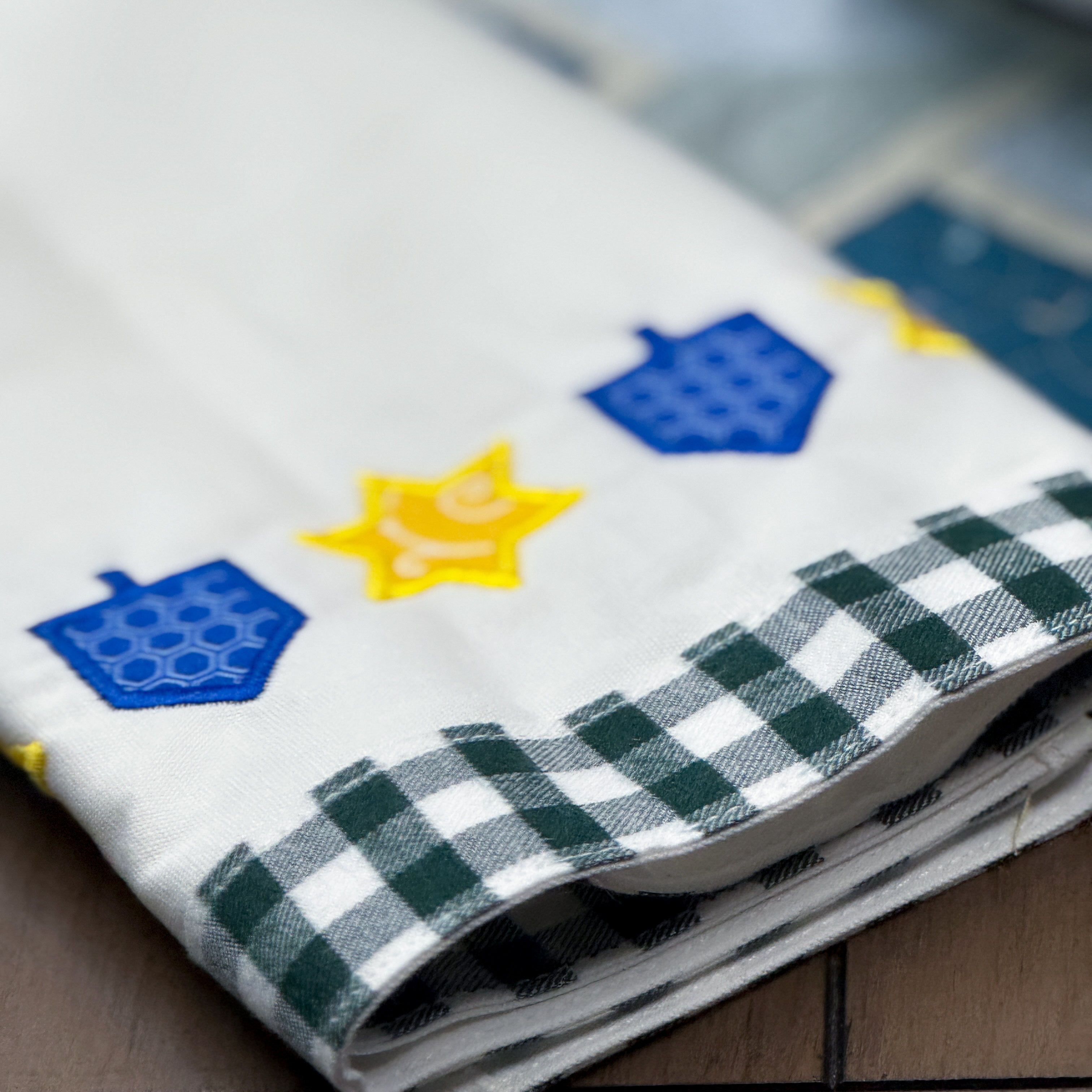 Folded fabric with blue and yellow embroidered designs on a checkered border.