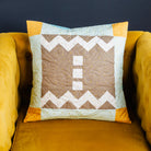 Quilted pillow with geometric pattern on a mustard yellow armchair against a dark background