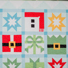 Quilt block with star, house, and bow designs in red, green, blue, and yellow on a light background.