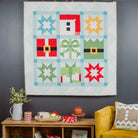 Colorful quilt hanging on a dark wall above a wooden shelf with decorative items and a yellow chair.