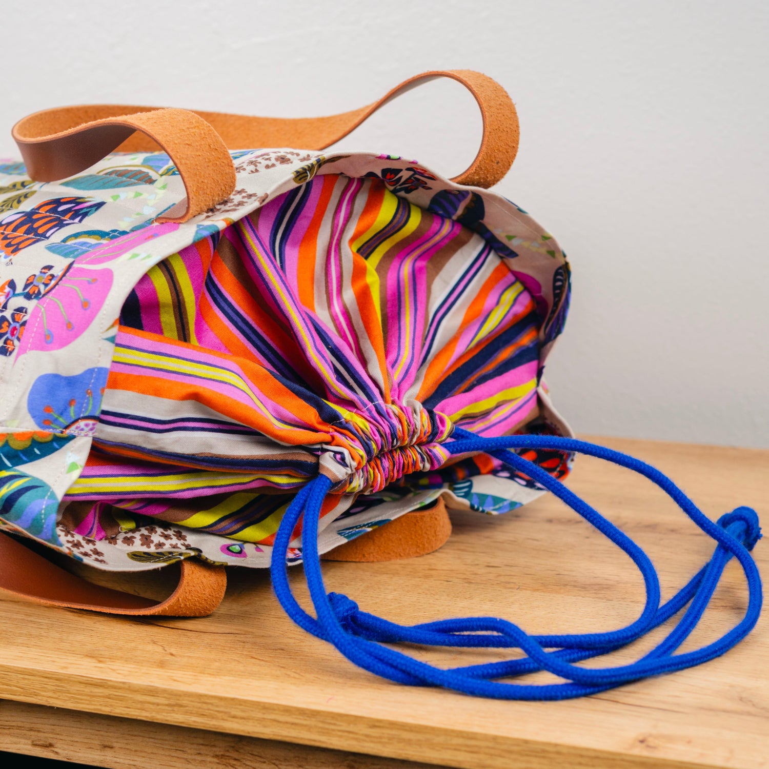 Colorful drawstring bag with a blue strap on a wooden surface
