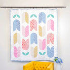 Colorful quilt with abstract pattern hanging on a wall next to a yellow chair.