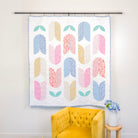 Colorful abstract patterned wall hanging above a yellow armchair in a room.