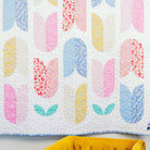 Colorful quilt with abstract pattern on a white wall with a yellow chair and blue flowers.