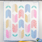 Colorful quilt with floral patterns hanging on a wall above a yellow chair.
