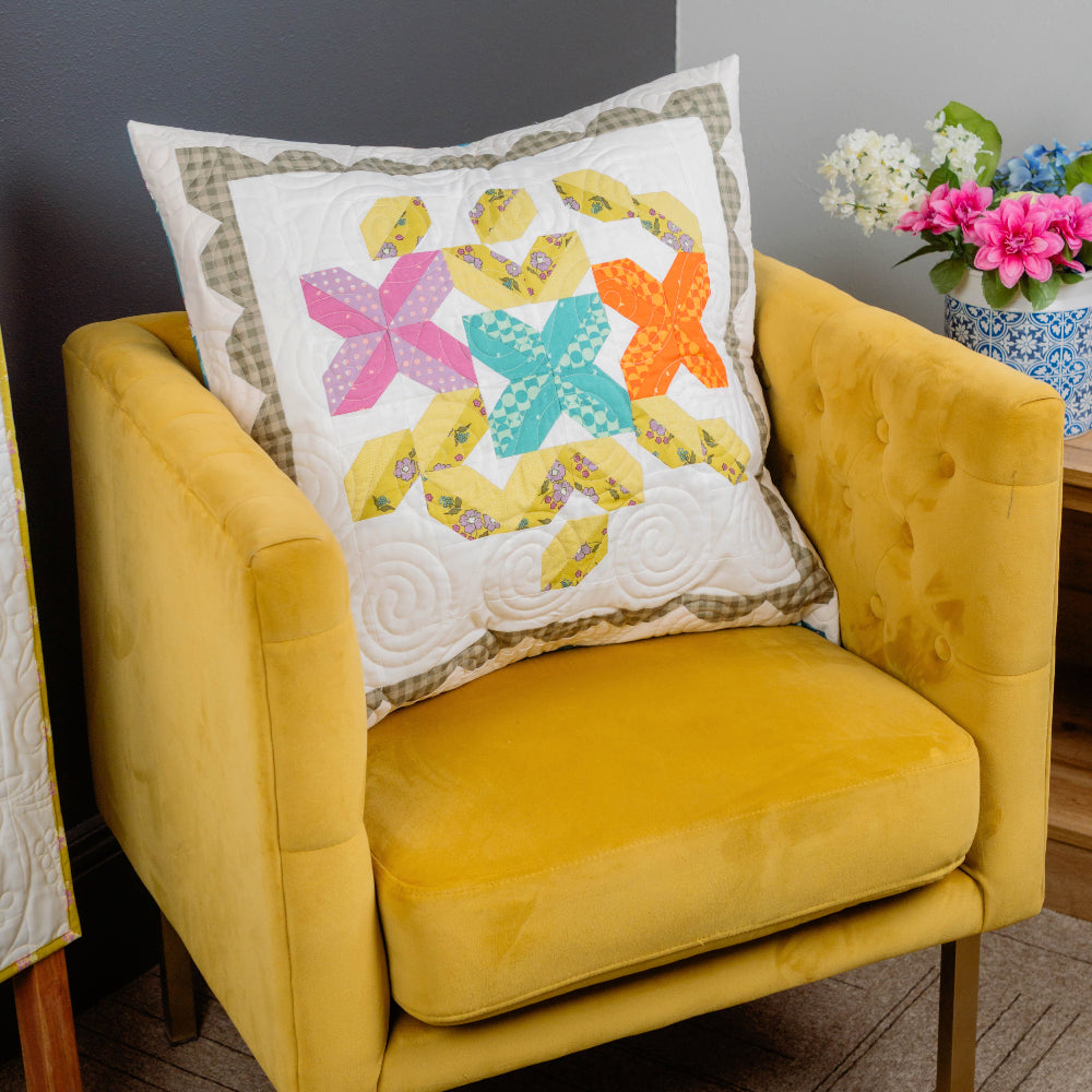 Yellow armchair with a colorful butterfly-patterned pillow against a gray wall.