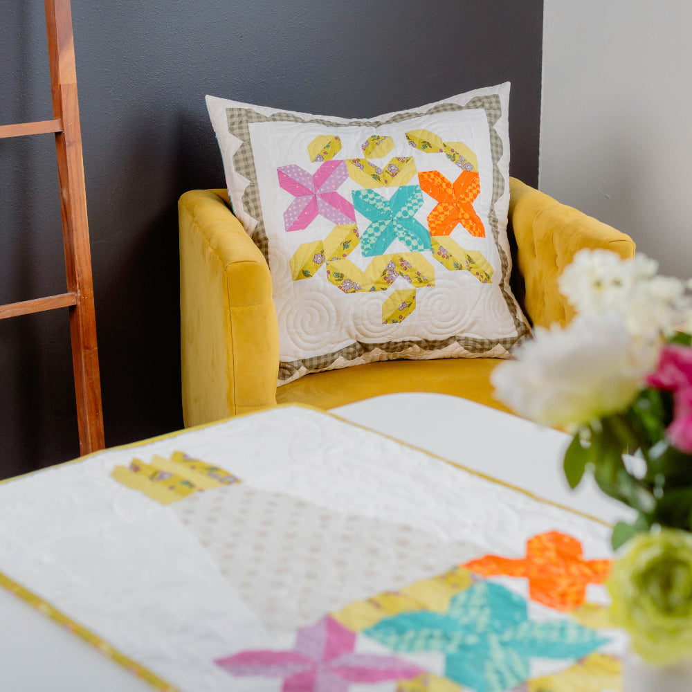 Decorative pillow with floral patterns on a yellow chair next to a vase of flowers.