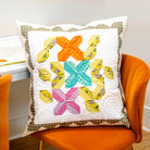 Quilted pillow with colorful butterfly pattern on an orange chair.