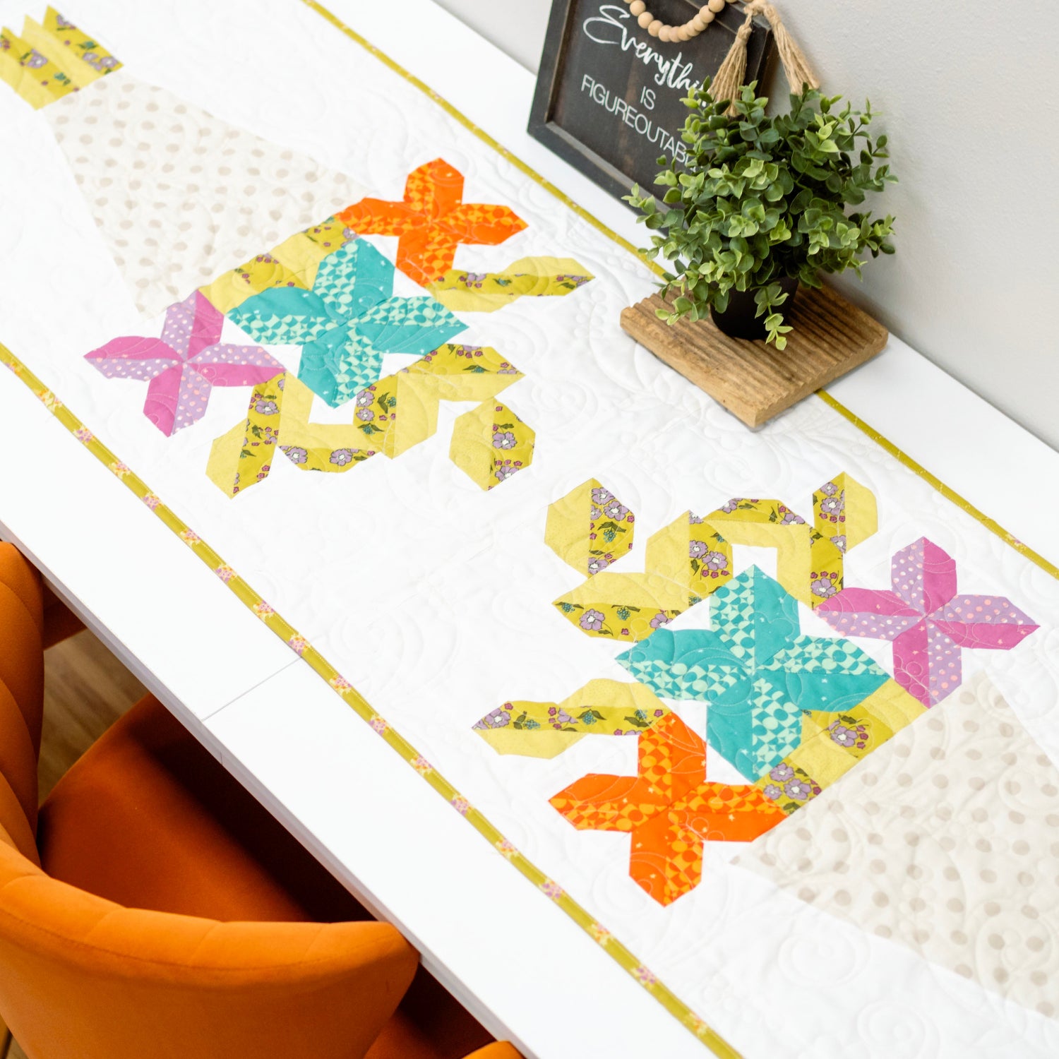 Colorful starfish patterned table runner on a dining table with orange chairs and a plant in the background.