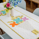 Dining table with a colorful quilted table runner and floral arrangement.