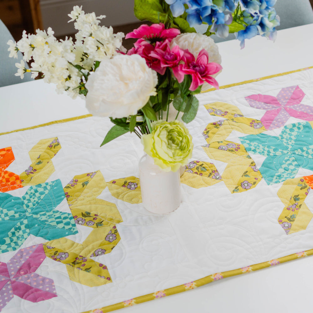 Colorful floral arrangement in a vase on a table with a patchwork tablecloth.