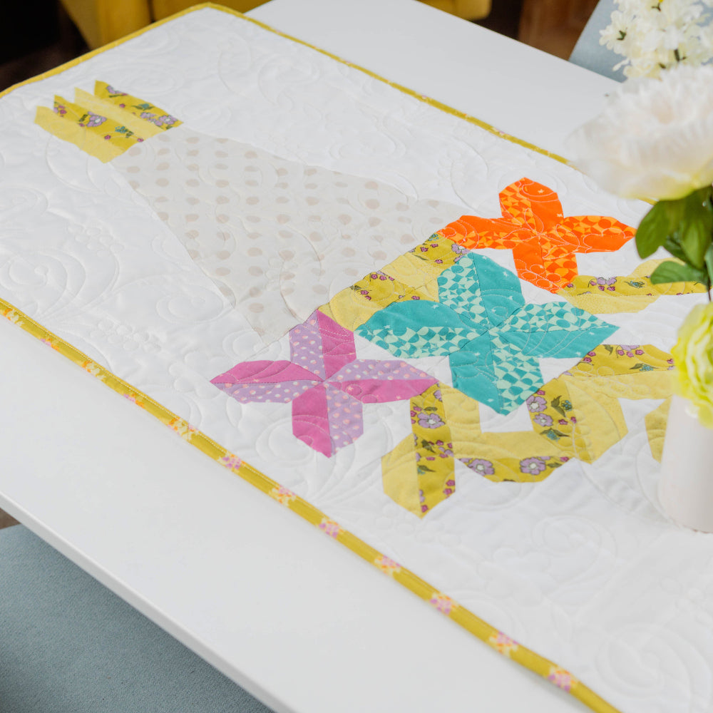 Colorful quilted table runner on a dining table with flowers.