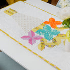 Colorful quilted table runner on a dining table with flowers.