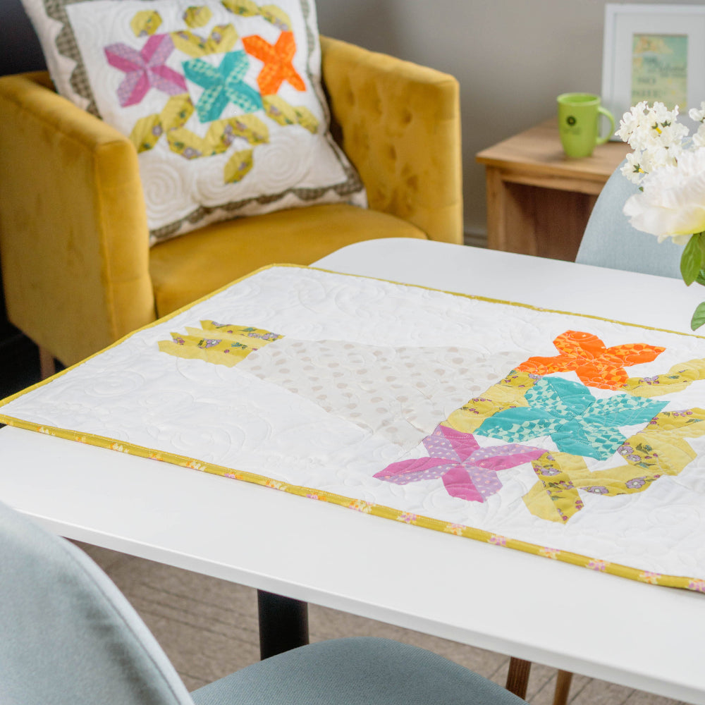 Colorful quilt with butterfly design on a table in a room with a yellow chair and floral pillow.
