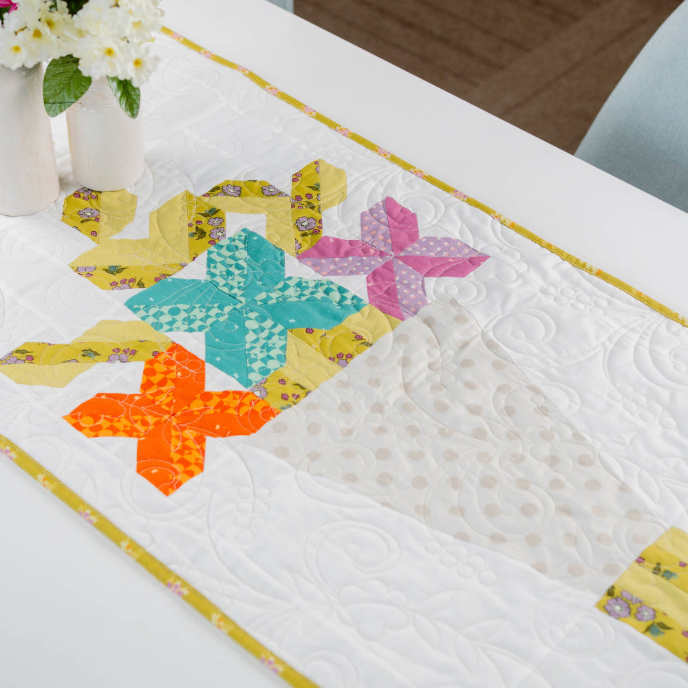 Colorful quilted table runner with star patterns on a white surface.