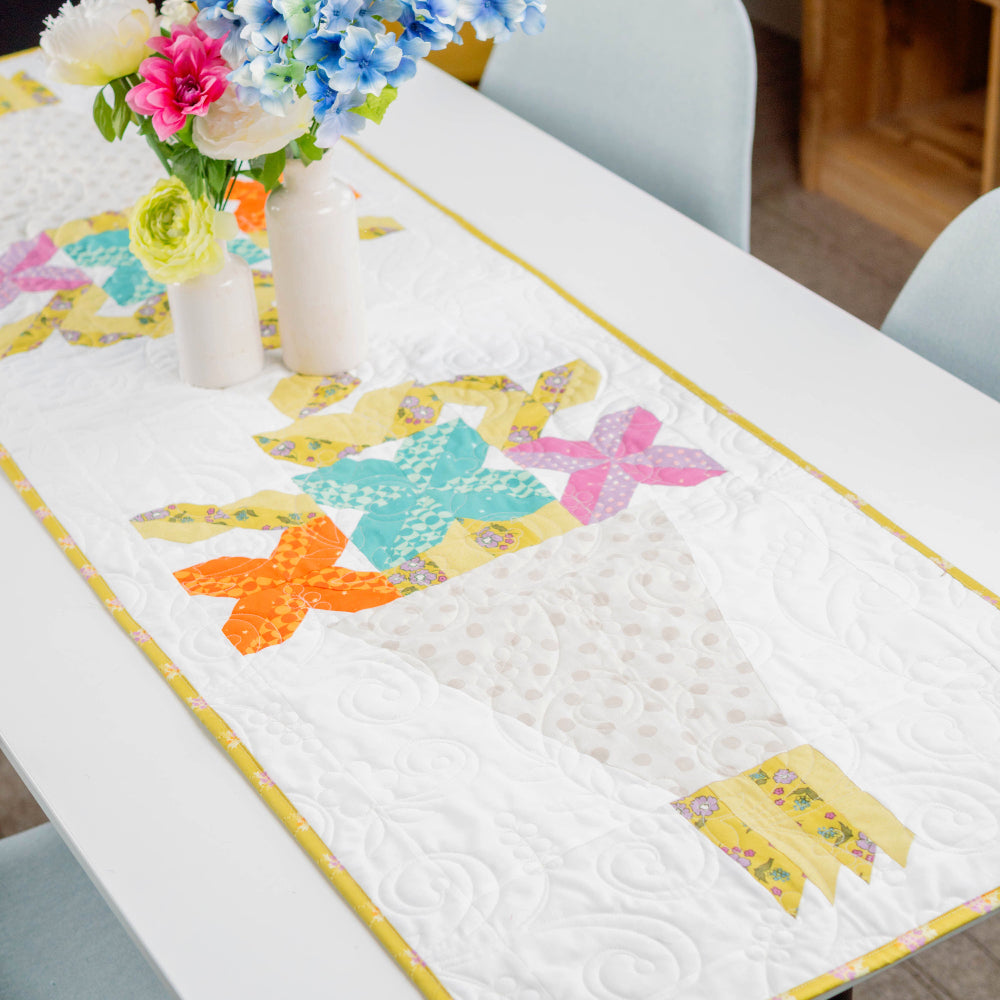 Colorful table runner with butterfly design on a dining table, accompanied by flowers.