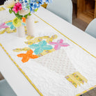 Colorful table runner with butterfly design on a dining table, accompanied by flowers.