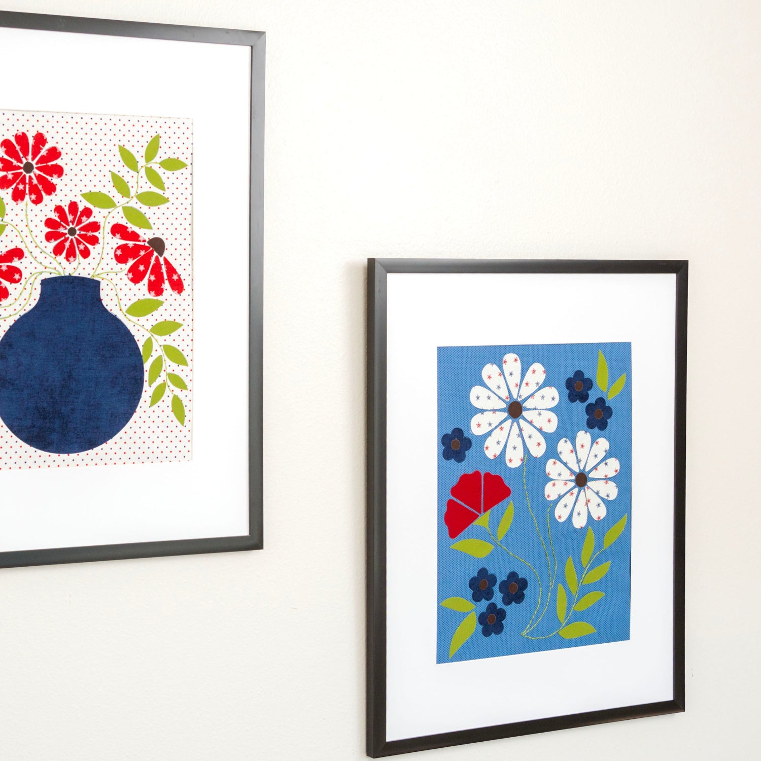 Two framed artworks on a white wall, one with red and blue floral design and the other with white flowers on a blue background.