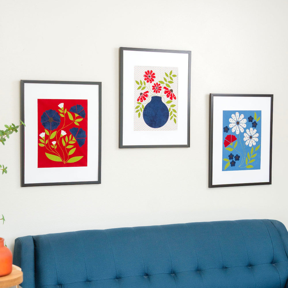 Three framed floral artworks on a wall above a blue sofa.