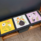 Three floral quilted placemats on a wooden table against a dark background