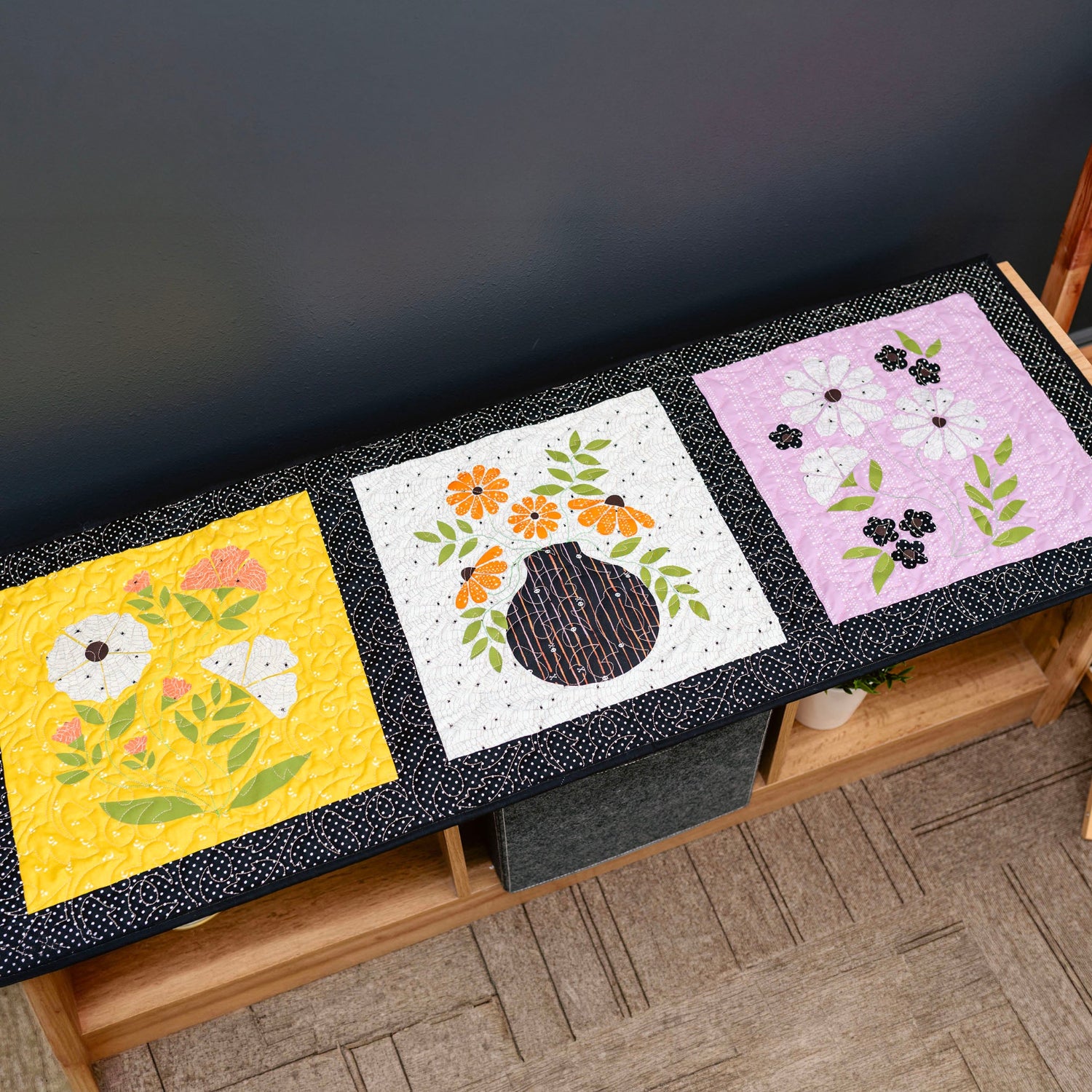 Three floral quilted placemats on a wooden table against a dark background