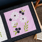 Two quilted blocks with floral designs on a wooden surface.