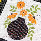 Quilt block with a black vase and orange flowers on a white background