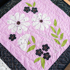 Quilt square with white flowers, blackberries, and green leaves on a pink background
