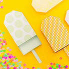 Decorative paper ice cream cones with polka dot patterns on a yellow background with colorful confetti.