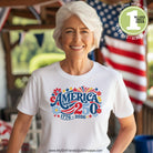Woman wearing a white t-shirt with 'America 250' design in front of an American flag.