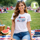 Woman wearing a white t-shirt with 'America 250' design, sitting on a picnic blanket outdoors.