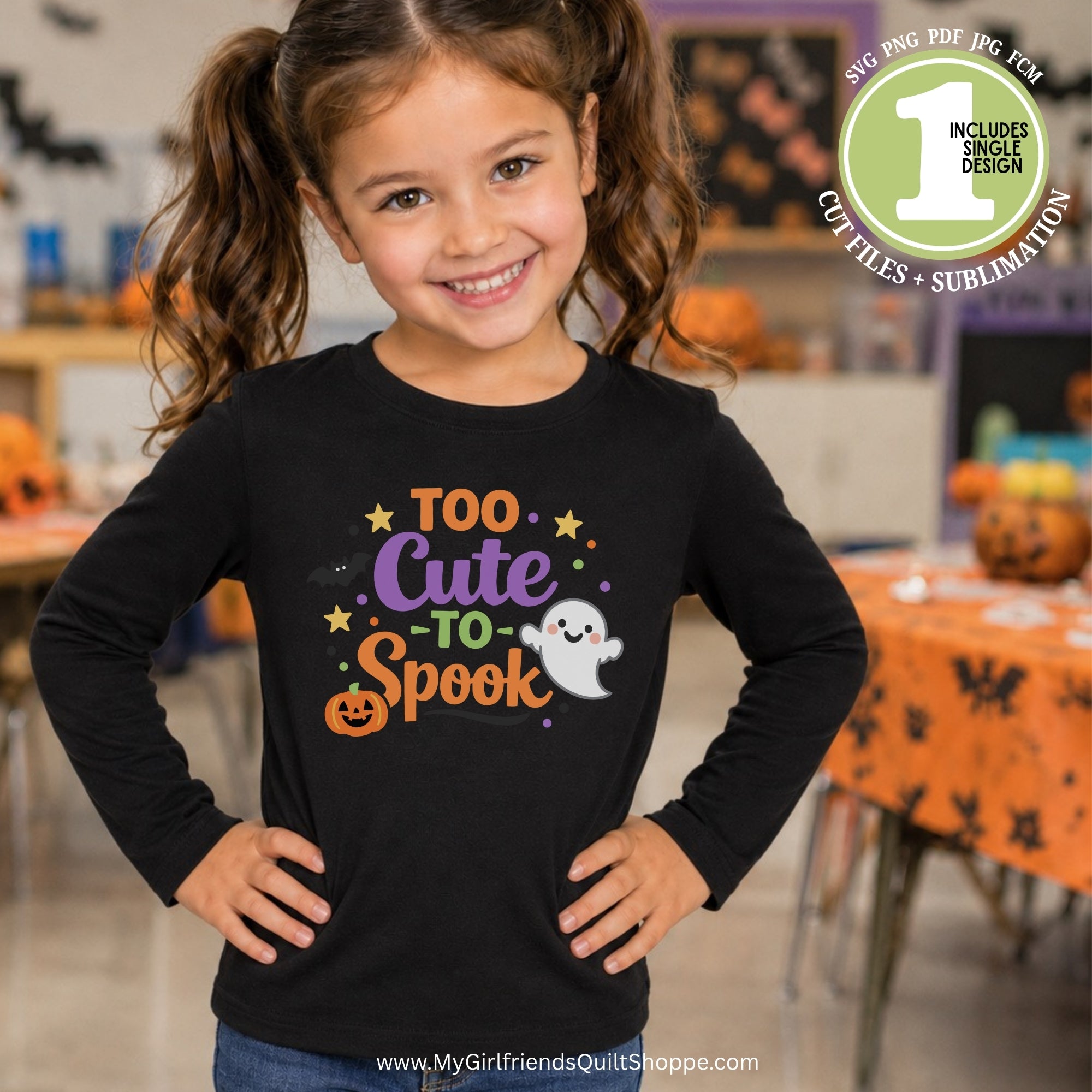 A young girl with brown pigtails smiles while wearing a black long-sleeve shirt with a colorful 'Too Cute to Spook' Halloween graphic. The graphic features orange text, a jack-o'-lantern, purple text, yellow stars, and a white ghost.