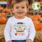 A smiling toddler wearing a white long-sleeve shirt with a 'Cuteest Pumpkin in the Patch' autumn graphic, posed in front of a blurred pumpkin patch with hay bales. A green circular badge in the top right advertises digital design files.