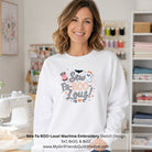 A smiling woman stands in a sewing room wearing a white crewneck sweatshirt with a colorful graphic that reads 'Sew Fa-BOO-Lous!' with a spool of thread, ghost, bat, and pumpkin details. A sewing machine is visible on the left, and shelves of fabrics and thread are in the background.