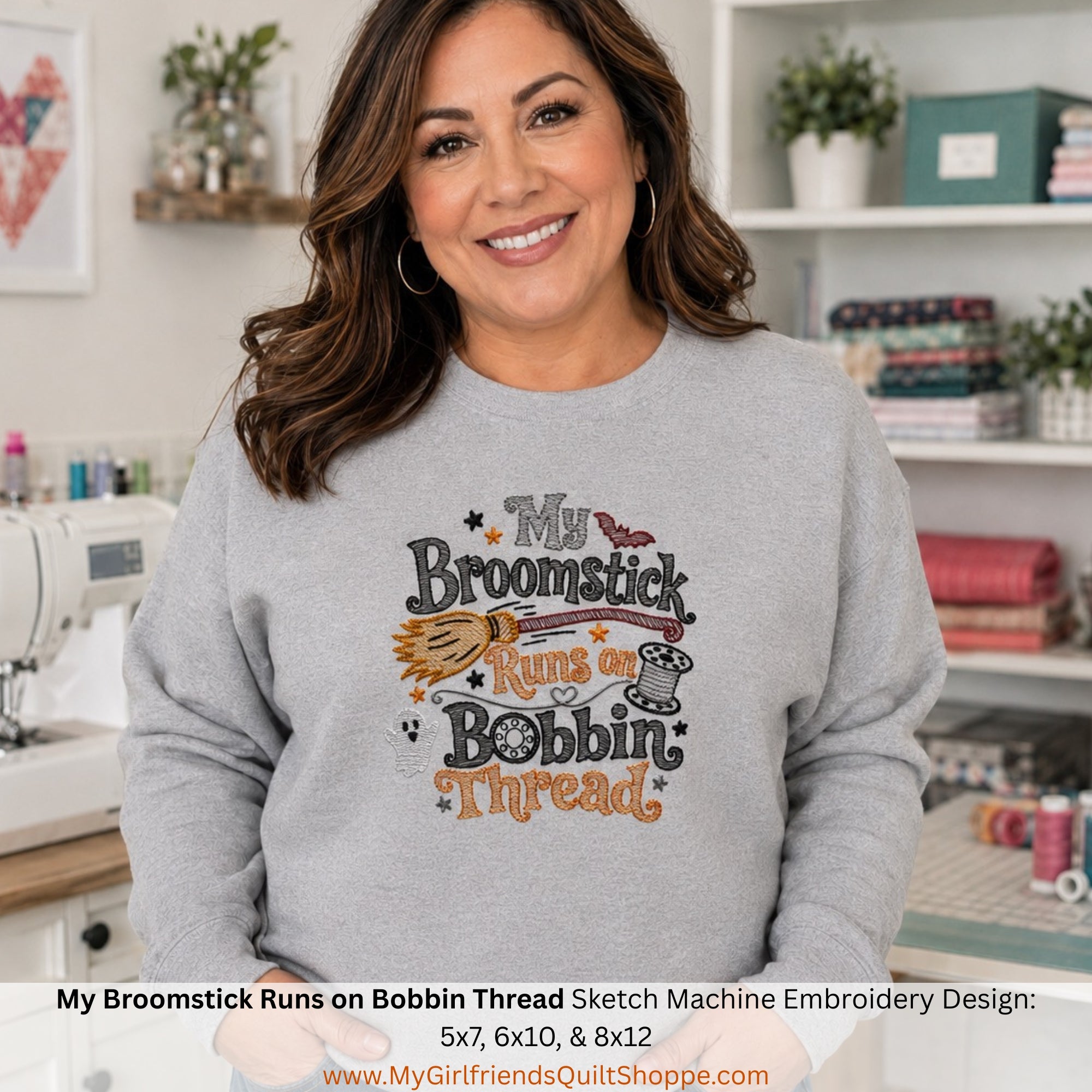 A smiling woman wearing a light gray crewneck sweatshirt with a colorful embroidered-style graphic that reads 'My Broomstick Runs on Bobbin Thread.' The photo is taken in a bright sewing room with shelves, fabric, and a sewing machine visible in the background.