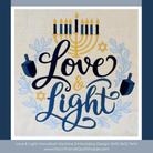 A square machine embroidery design preview featuring the words “Love & Light” in dark navy and blue script, with a gold menorah at the top, blue floral accents, and two blue dreidels on a light beige fabric background. The design is centered within a white border, with a dark blue outer background and text at the bottom reading “Love & Light Hanukkah Machine Embroidery Design: 6x10, 8x12, 9x14” and “www.