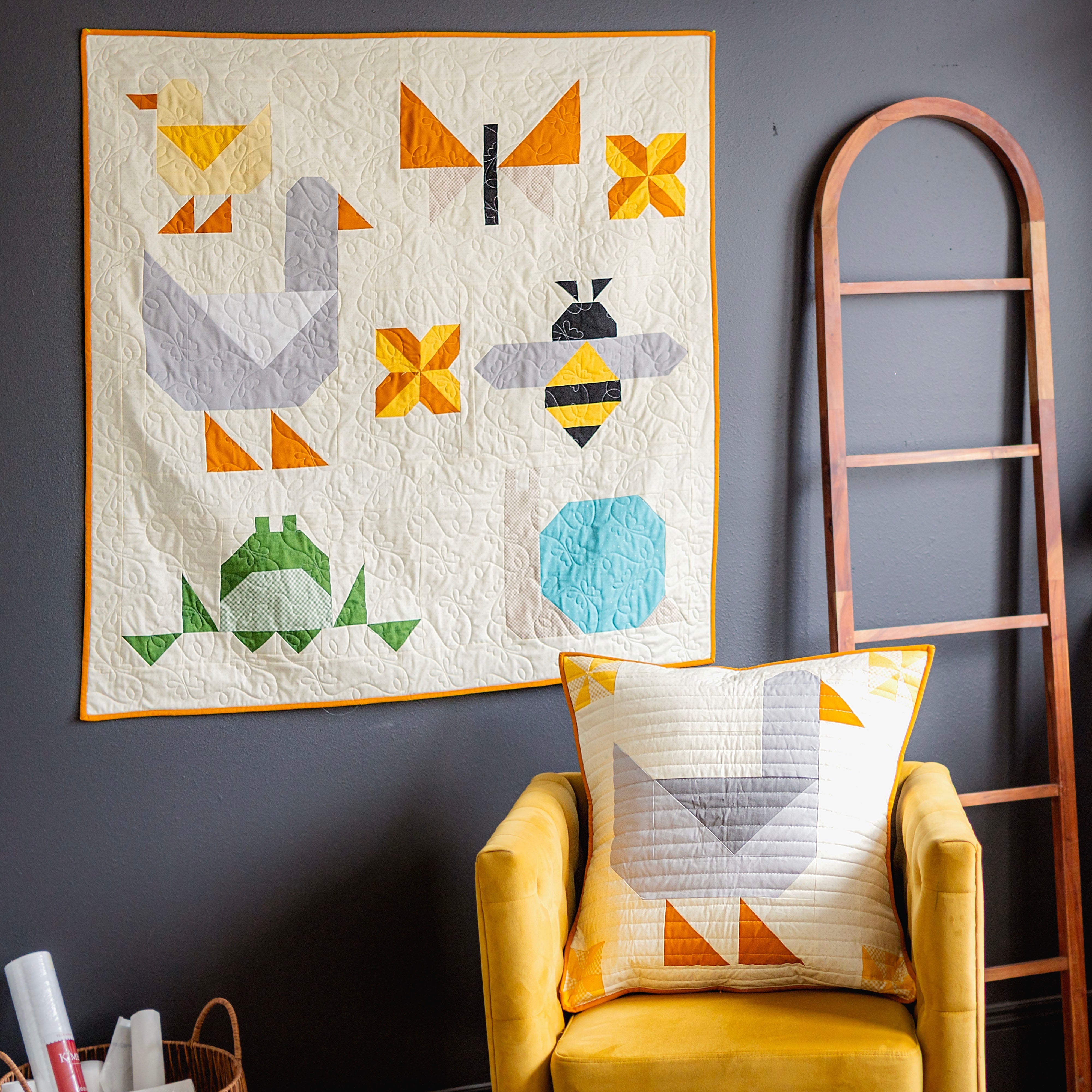 Quilt with geometric patterns on a wall above a yellow chair with a matching pillow.