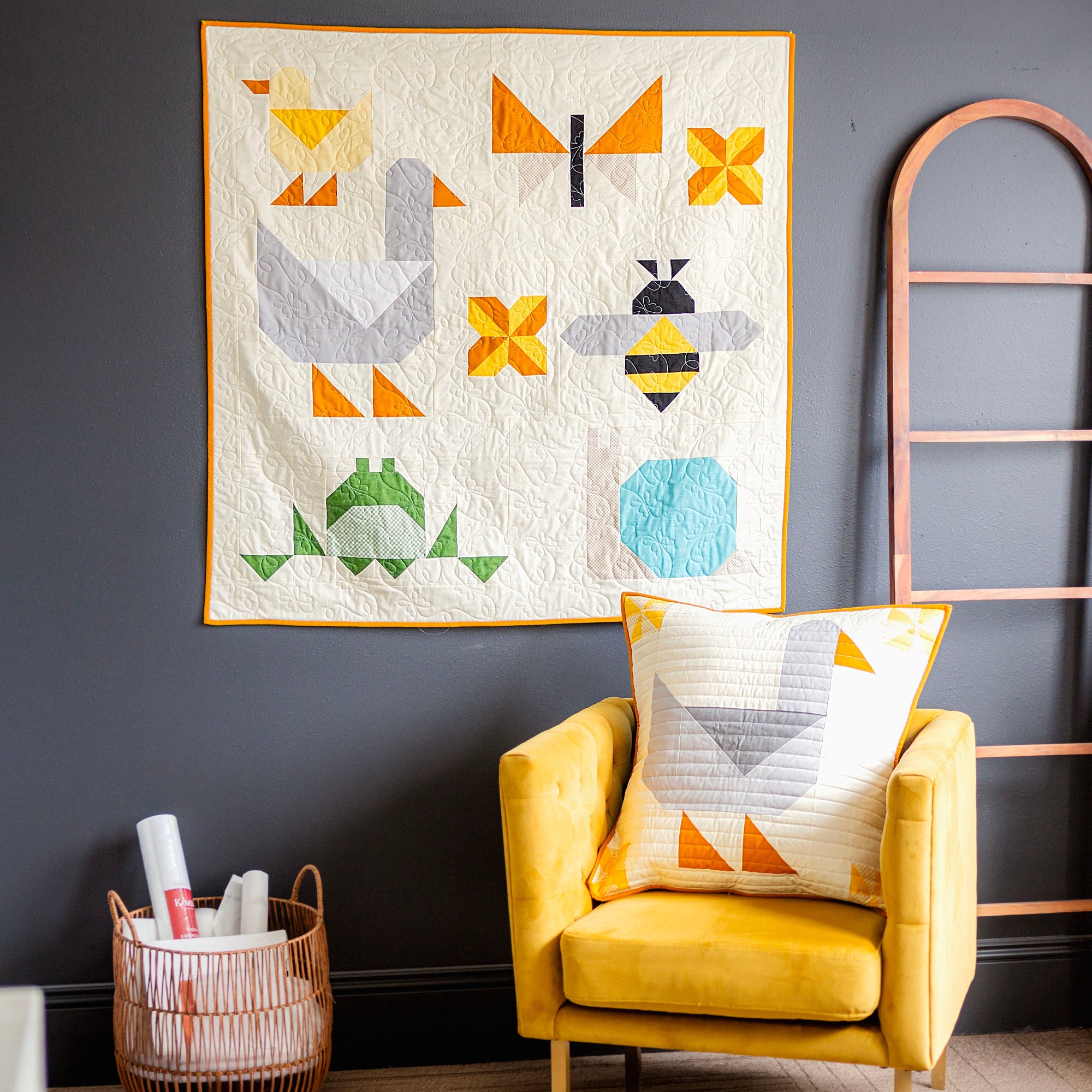 Animal Quilt with geometric patterns on a wall above a yellow chair with a matching goose pillow.