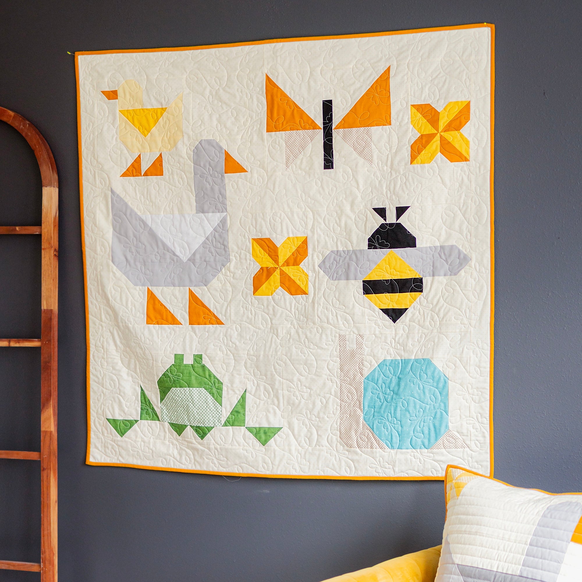 Colorful quilt with geometric animal patterns on a dark wall, yellow chair, and decorative pillows.