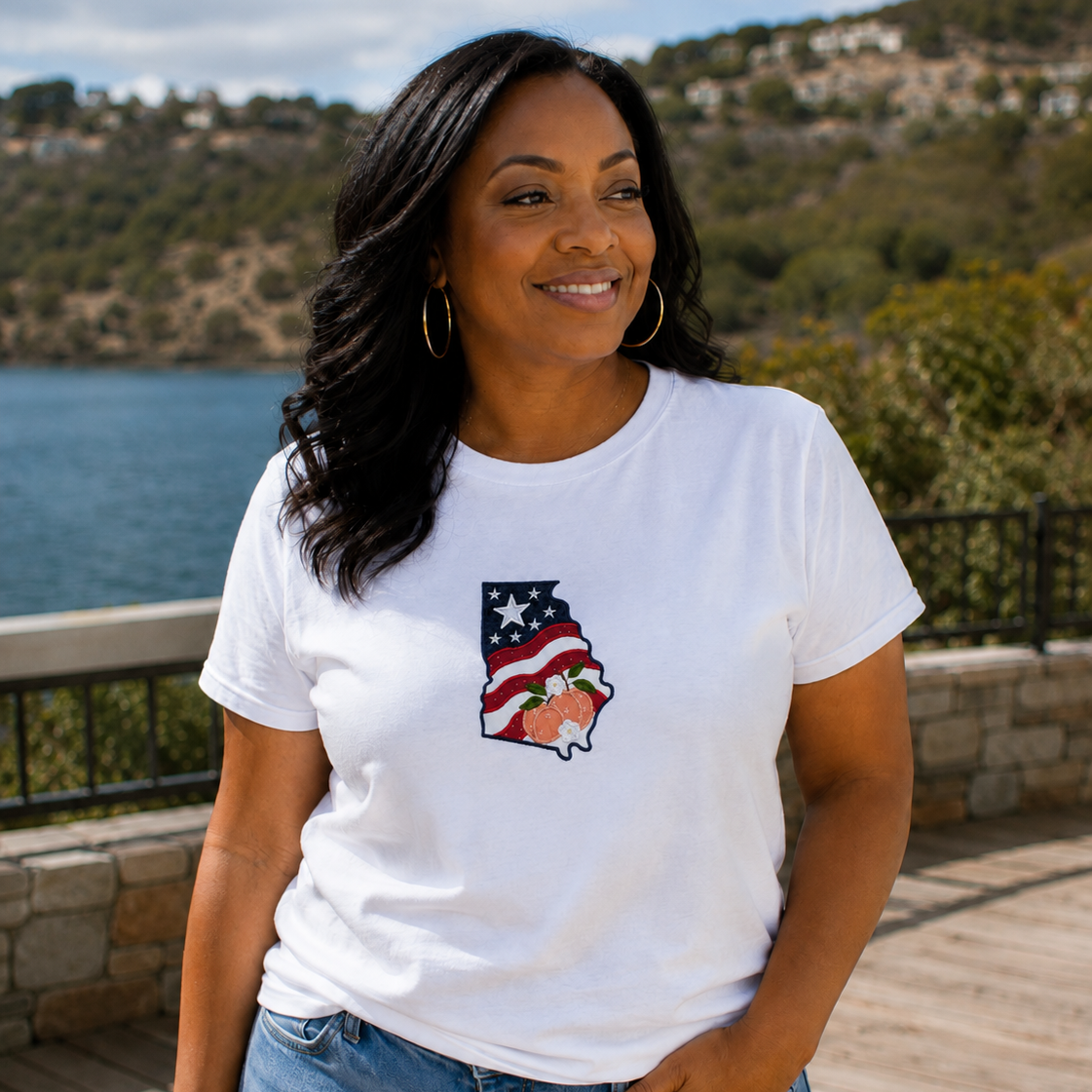 Woman wearing a white t-shirt with a graphic design, standing outdoors near a body of water.